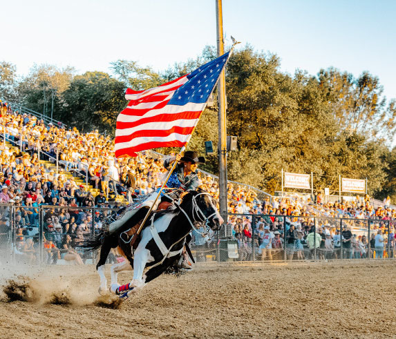 cowgirl riding horse while carrying the American Flag